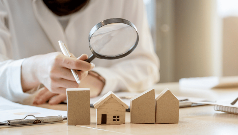 A person looking at wooden toy houses through a magnifying glass