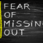 A Blackboard with FOMO written vertically in yellow and "Fear of missing out written horizontally in white to spell out the meaning