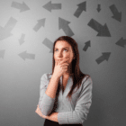 A woman in work attire standing with her arms crossed and one hand on her chin thinking deeply.